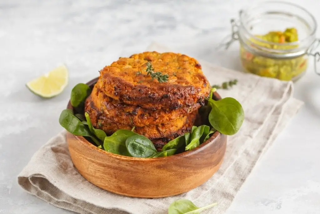 Hambúrguer de lentilha dentro de um recipiente de madeira com folhas de espinafre