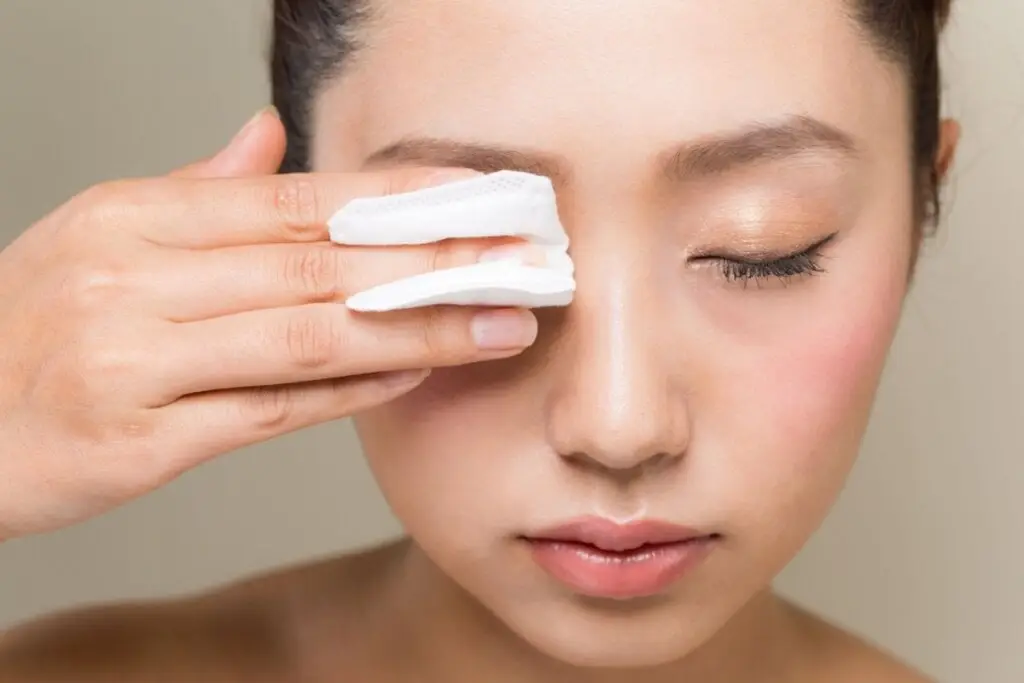 mulher de cabelo preso, olhos fechados e passando papel branco em um dos olhos