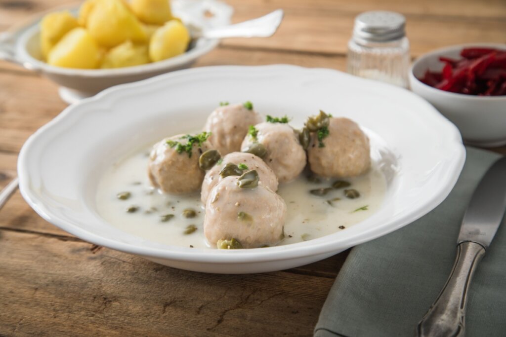 Prato branco com almôndega com molho de alcaparras em cima de uma mesa de madeira 