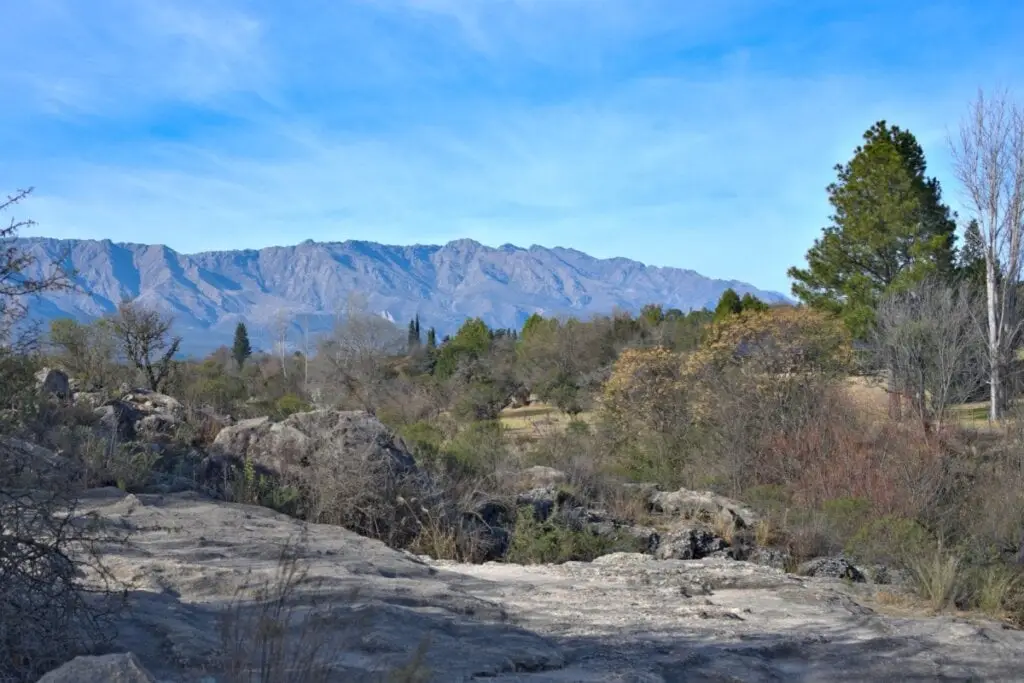 Paisagem com a cadeia de montanhas conhecida como Sierras de Córdoba, árvores e solo rochoso às margens do rio Cruz del Eje, na província de Córdoba, Argentina.
