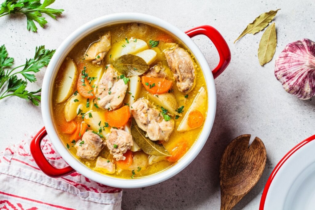 Sopa de frango com aveia e legumes em uma panela em cima de uma mesa branca