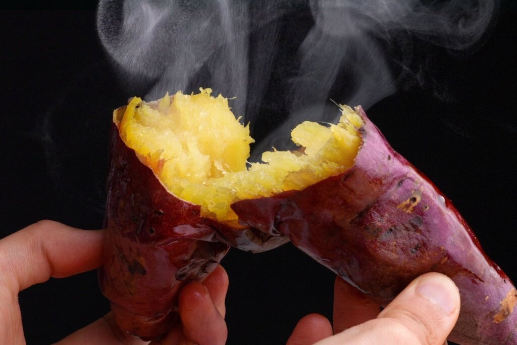 Uma batata-doce partida ao meio com fumaça saindo em fundo escuro