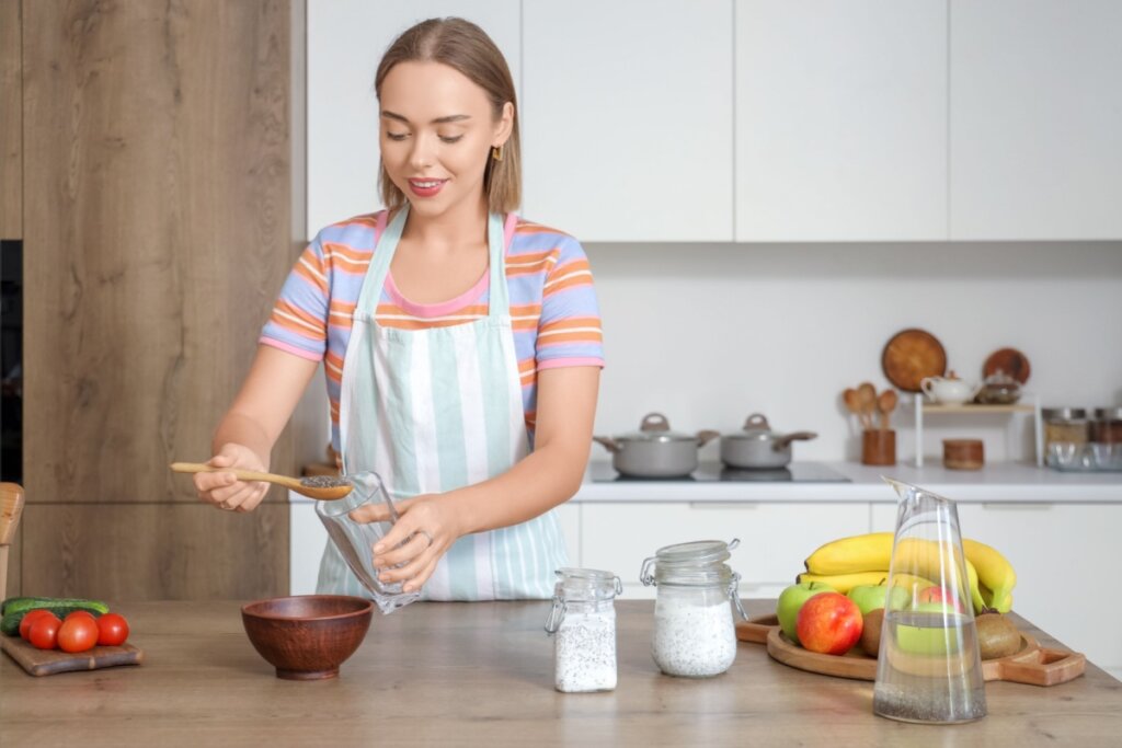 Mulher em uma cozinha, usando avental, colocando sementes de chia em um recipiente
