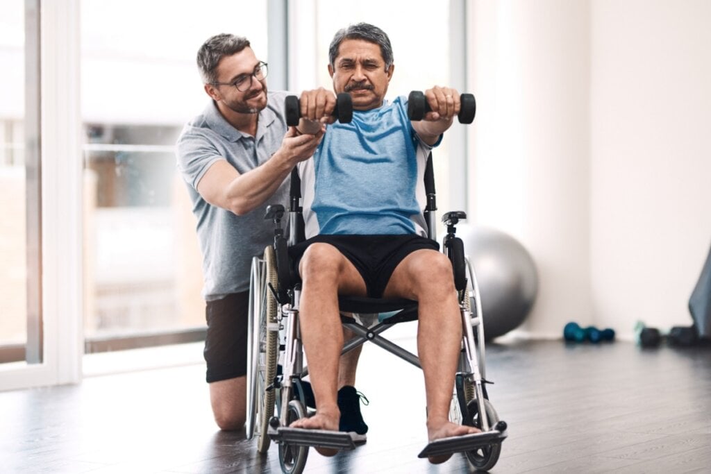 Fisioterapeuta auxiliando homem cadeirante durante exercício com halteres
