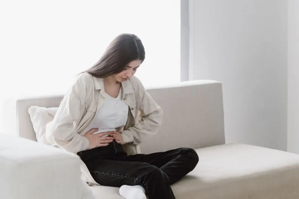 Mulher sentada inclinada com as duas mãos na barriga