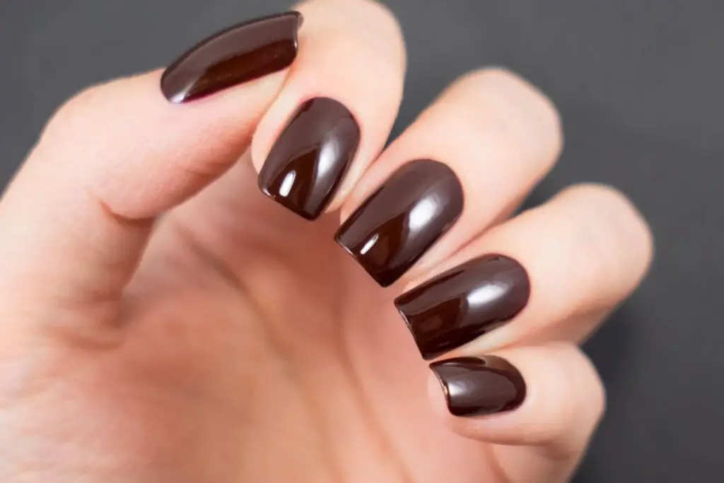 mão com unhas femininas em tom de marrom-escuro