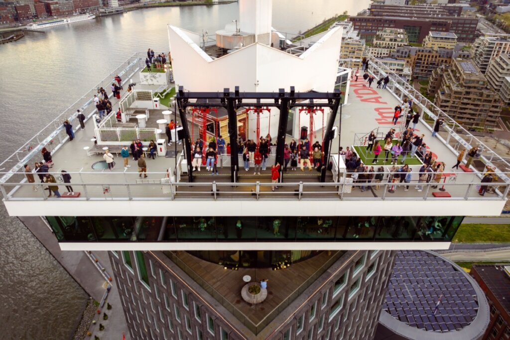Vista de cima de topo de prédio com pessoas circulando e um balanço em preto e vermelho