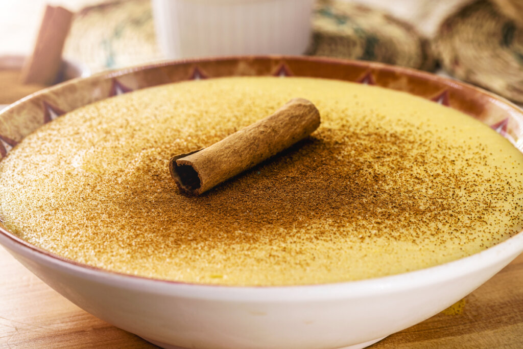 Curau de milho com canela em pó e em pau em recipiente branco