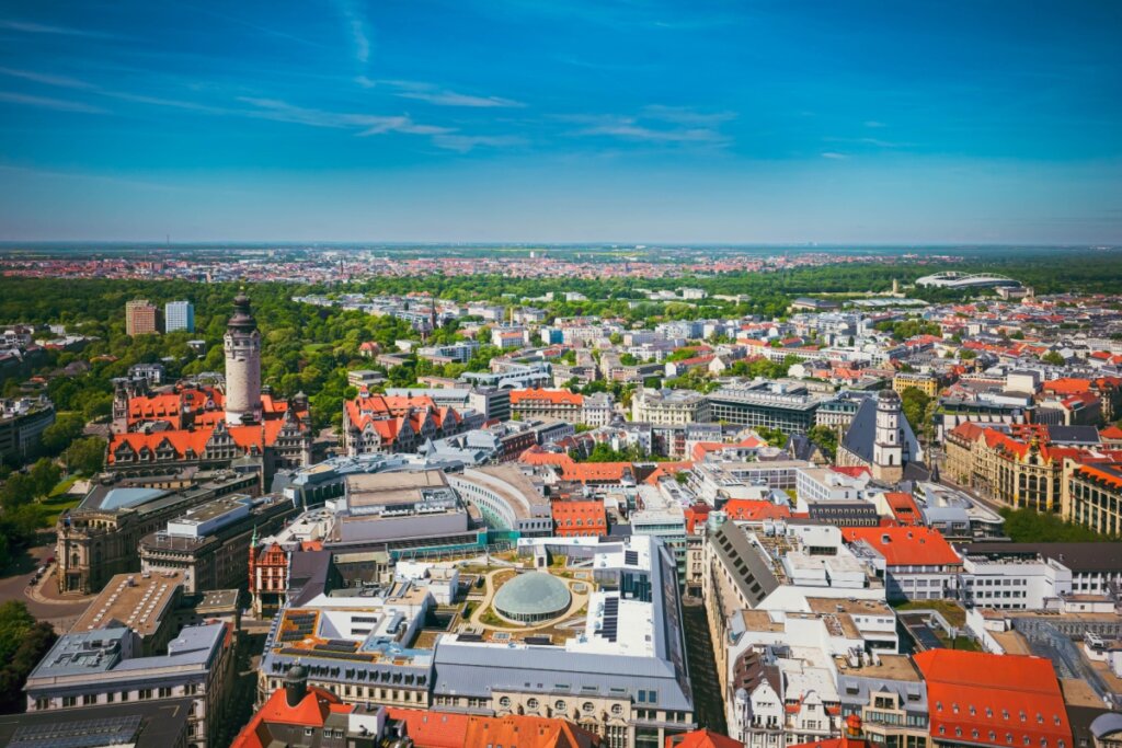 Imagem aérea da cidade de Leipzig com construções de tijolos, partes com árvores verdes e céu-azul