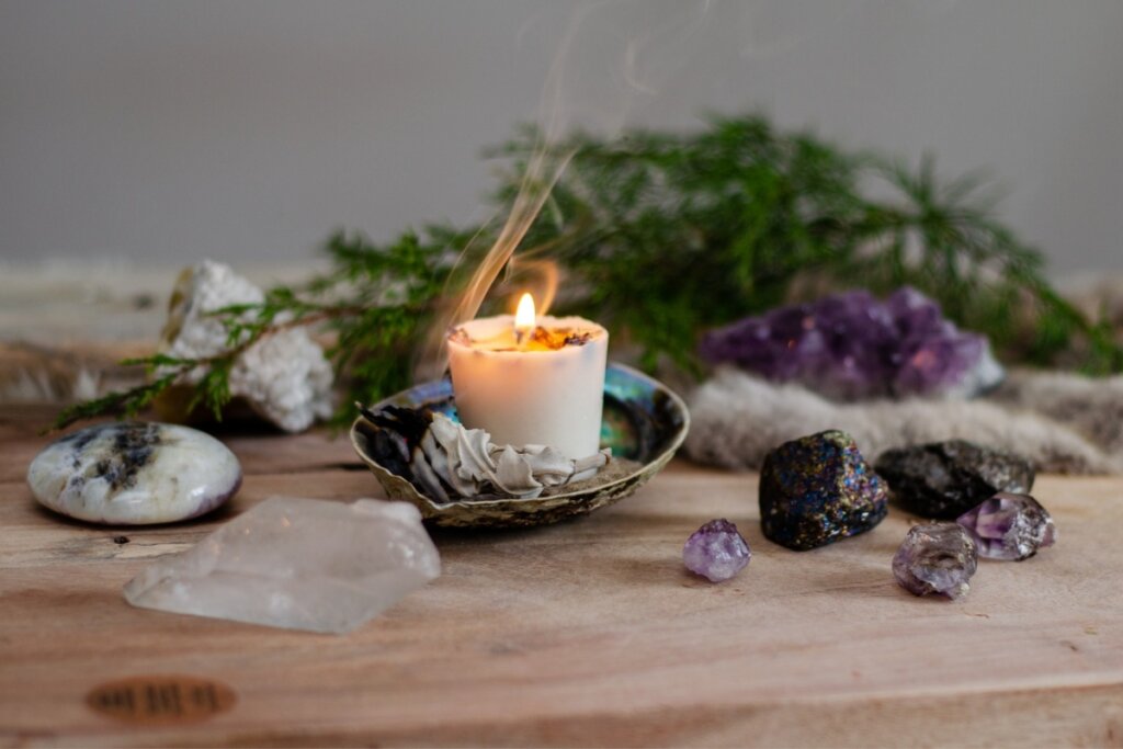 Vela branca acesa em uma mesa com cristais e erva verde