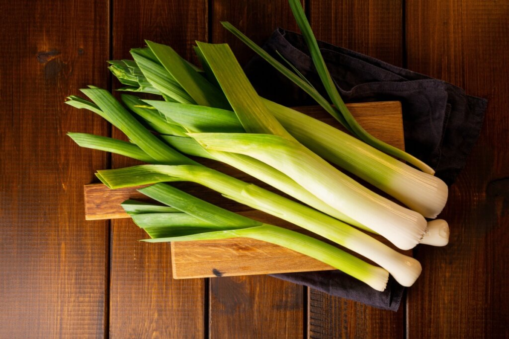 Alho-poró em cima de tábua de madeira em cima de mesa de madeiro e guardanapo de pano preto 
