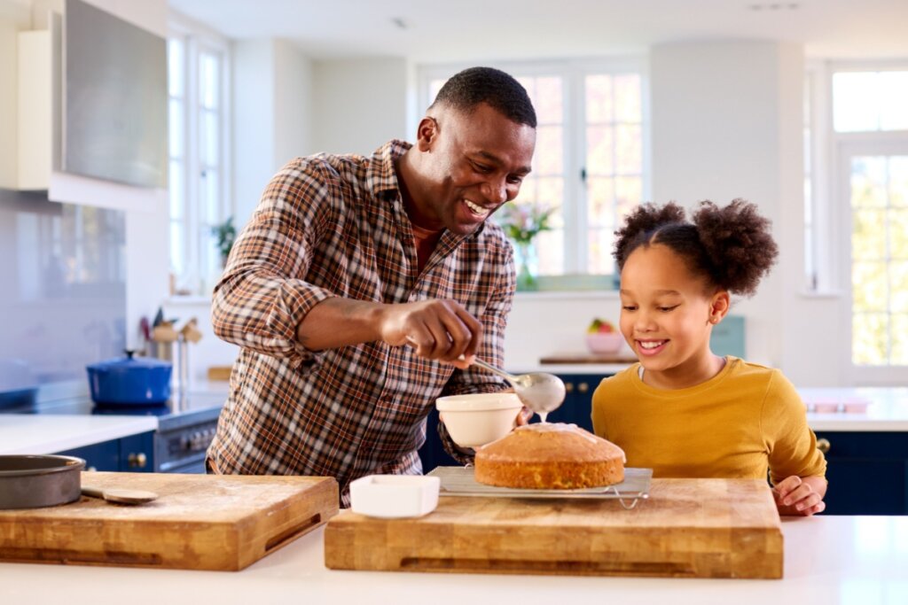 Pai e filha se divertindo juntos enquanto decoram um bolo na cozinha