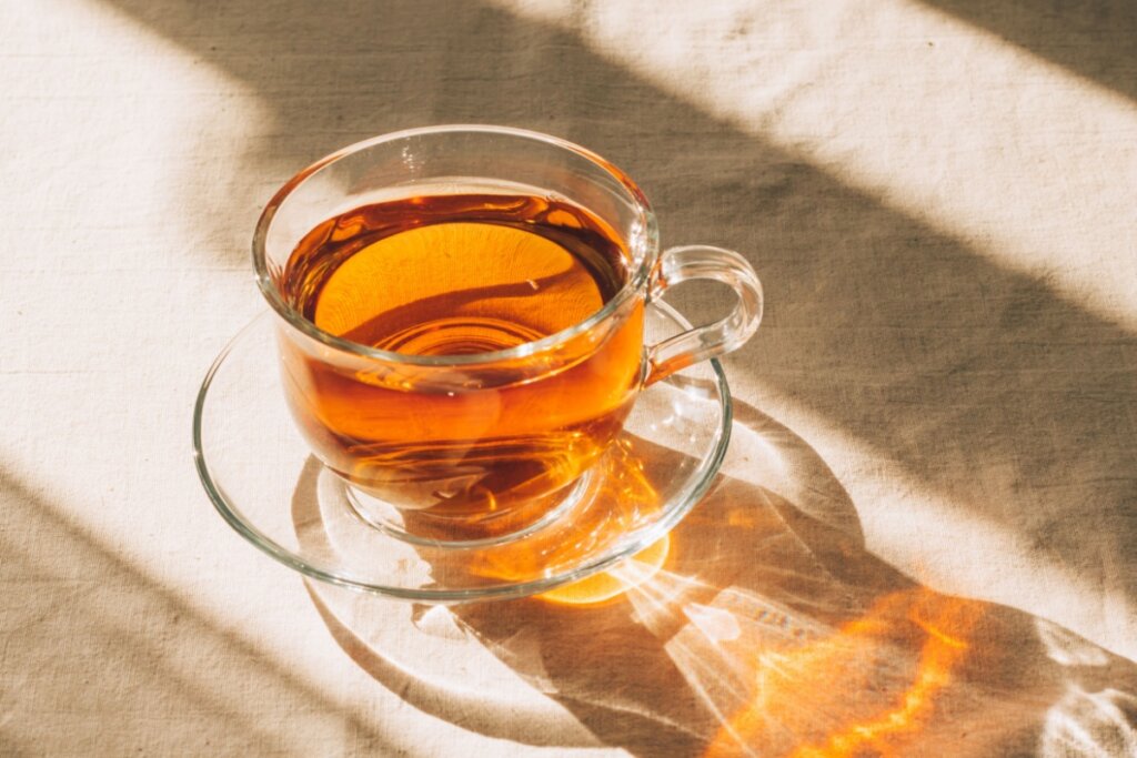 Xícara de vidro com chá em cima de um pano bege claro 
