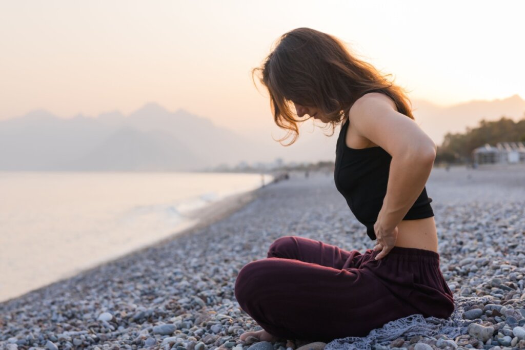 Mulher sentada em uma praia fazendo vácuo abdominal