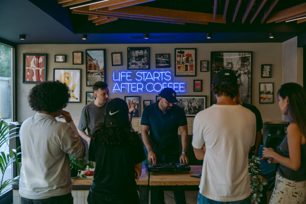 oito pessoas de costas em volta de mesa com DJ ao centro tocando