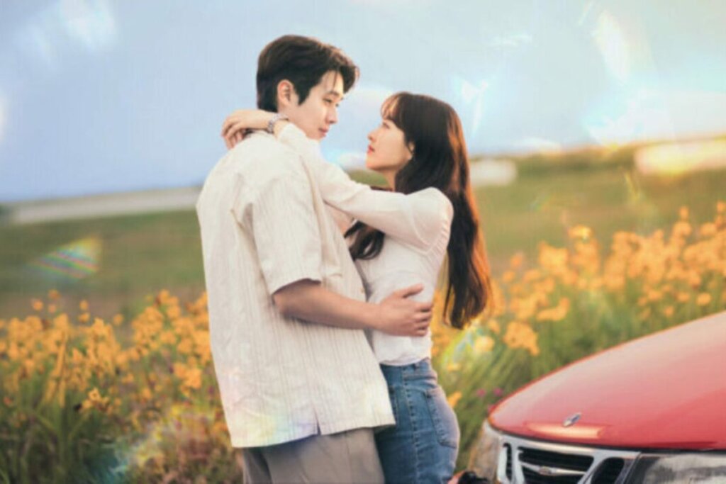 Protagonistas de "Um Amor de Cinema" abraçados um de frente para o outro em frente a um carro 