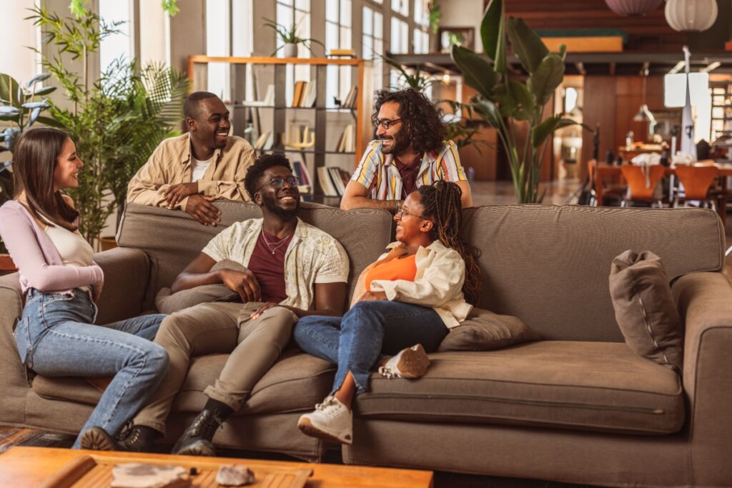 Cinco pessoas de diferentes origens conversando e rindo juntas em uma sala de estar compartilhada