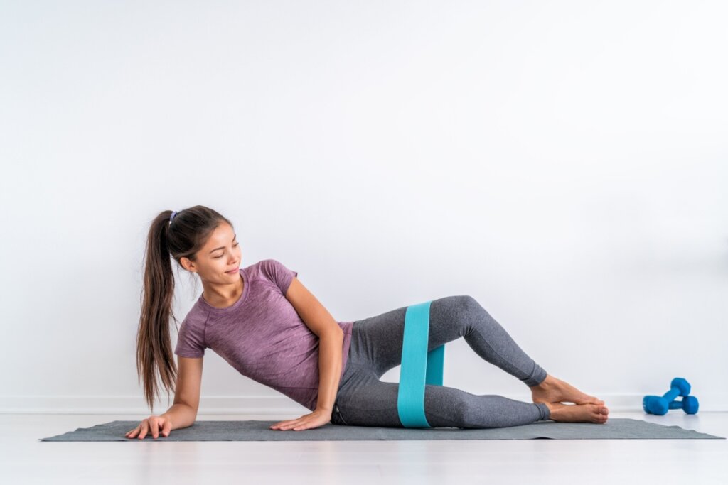 Mulher deitada com um mini band acima do joelho fazendo exercício de glúteo médio