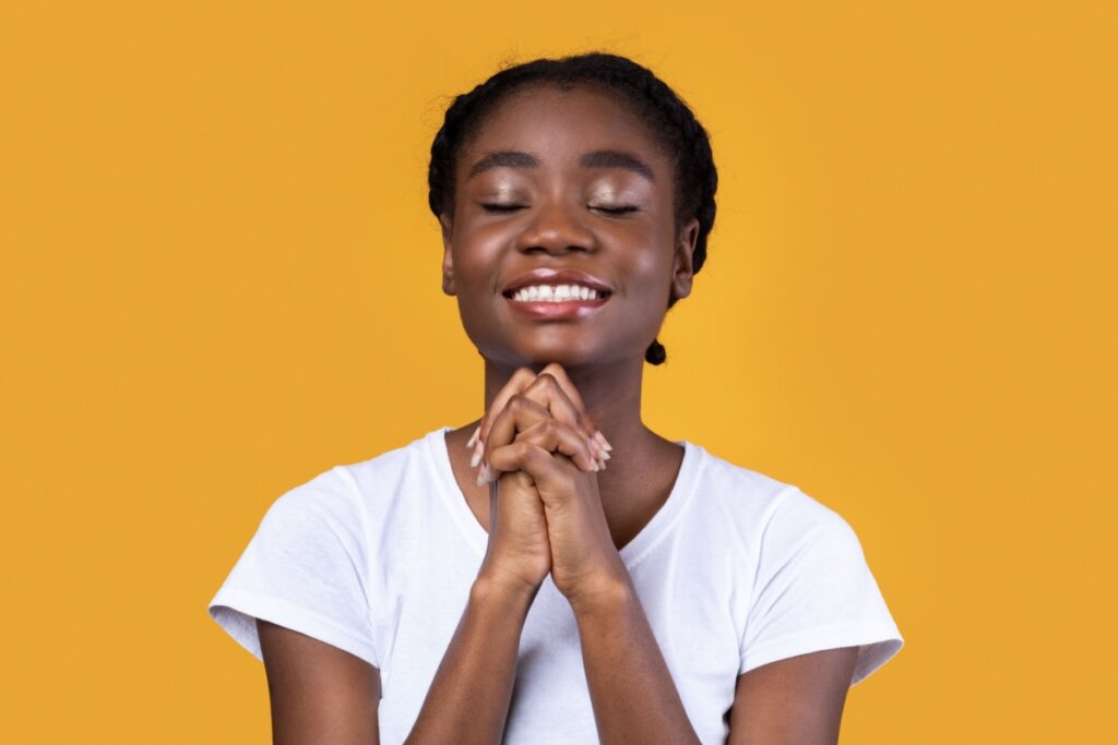 Mulher com os olhos fechados e as mãos juntas rezando