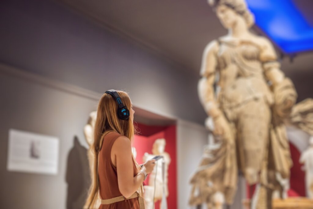 Mulher usando audiodescrição em um museu com estátuas a sua frente