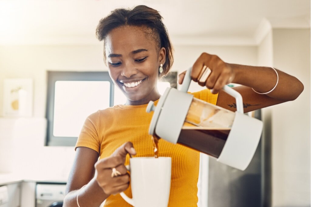 Mulher sorrindo e despejando café em uma xícara branca