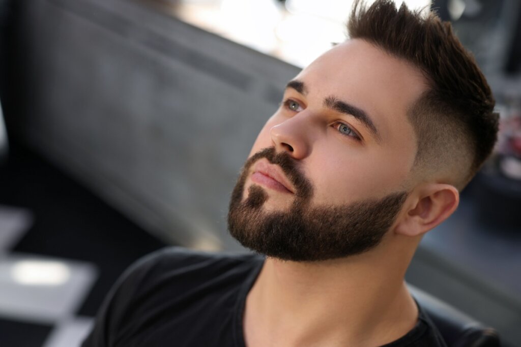 Homem com o cabelo curto e a barba curta feita modelando o rosto, usando camiseta preta