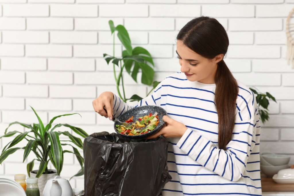 Mulher jogando sobras de comida orgânica em lixo orgânico com saco preto
