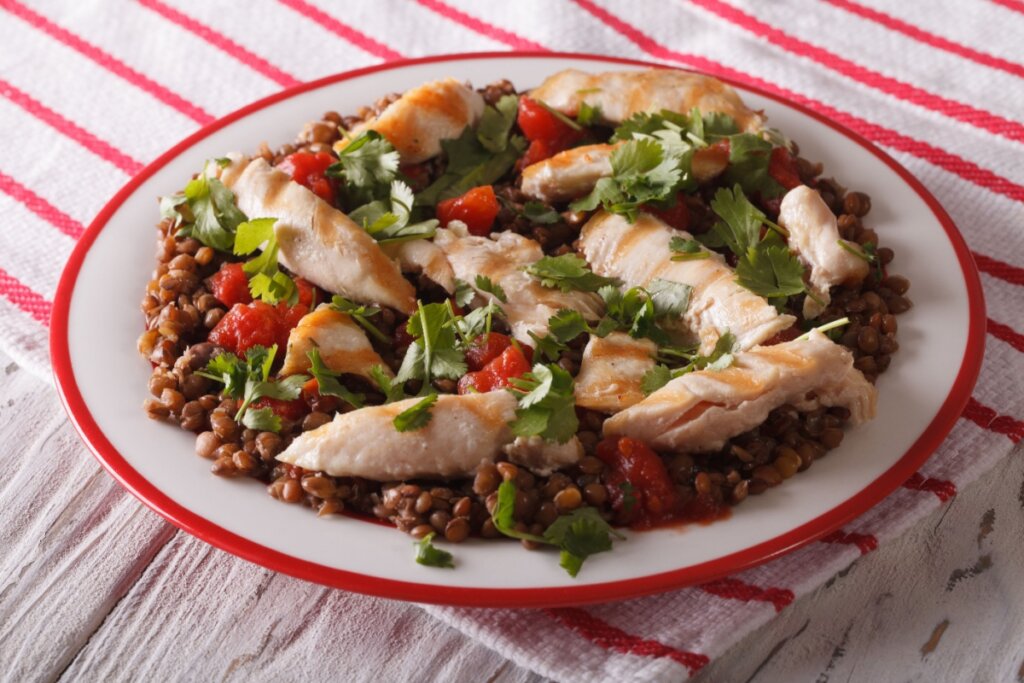 Prato raso com filé de frango grelhado em tiras sobre lentilhas cozidas, tomate em cubos e folhas frescas de coentro