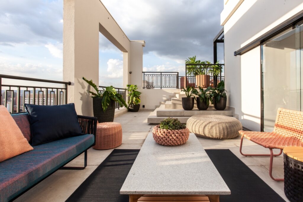 Área externa com mesa de centro em pedra, sofá, escada e plantas em vasos