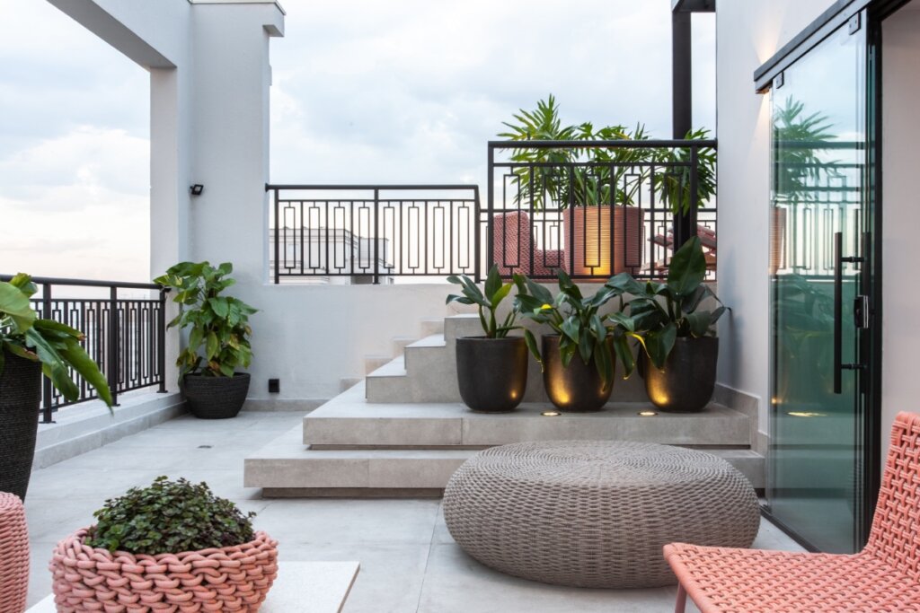 Varanda com escada cercada por vasos de plantas e pufe em trama natural