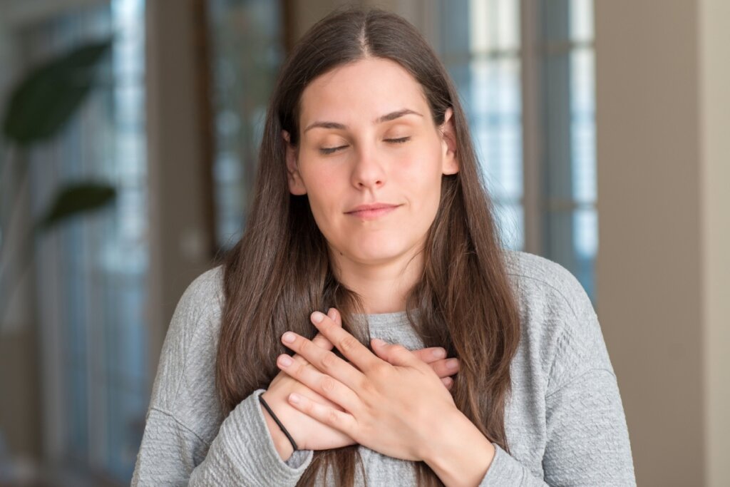 Mulher de cabelos castanhos e longos, soltos, com as duas mãos sobre o peito e os olhos fechados, em oração