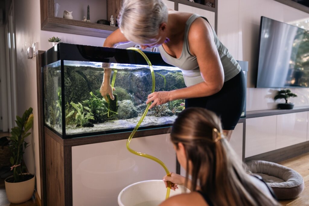 Mulher limpando um aquário com a ajuda de uma jovem que está agachada no chão