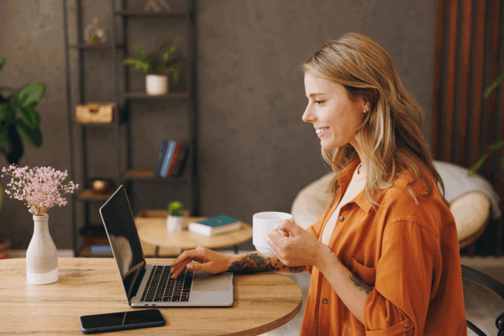 Mulher com cabelo loiro, curto, usando camisa de botões laranja mexendo no computador