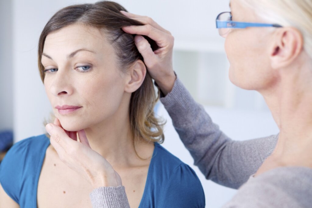 Mulher com cabelo curto, liso, usando camiseta azul, tendo o cabelo avaliado por médica em consultório