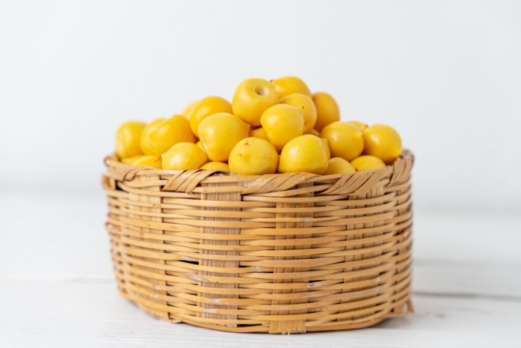 Cesto de vime com diversas frutas murici em cima de bancada de pedra branca em fundo branco