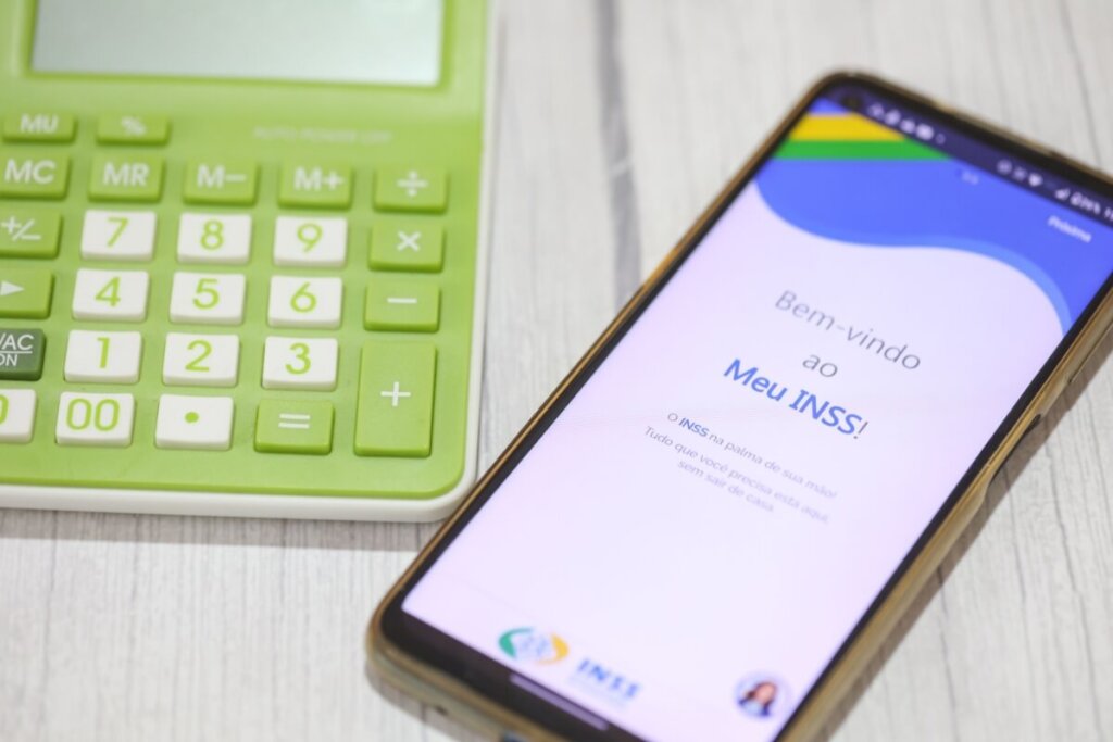 Celular com a tela aberta no aplicativo Meu INSS ao lado de uma calculadora verde sobre uma mesa