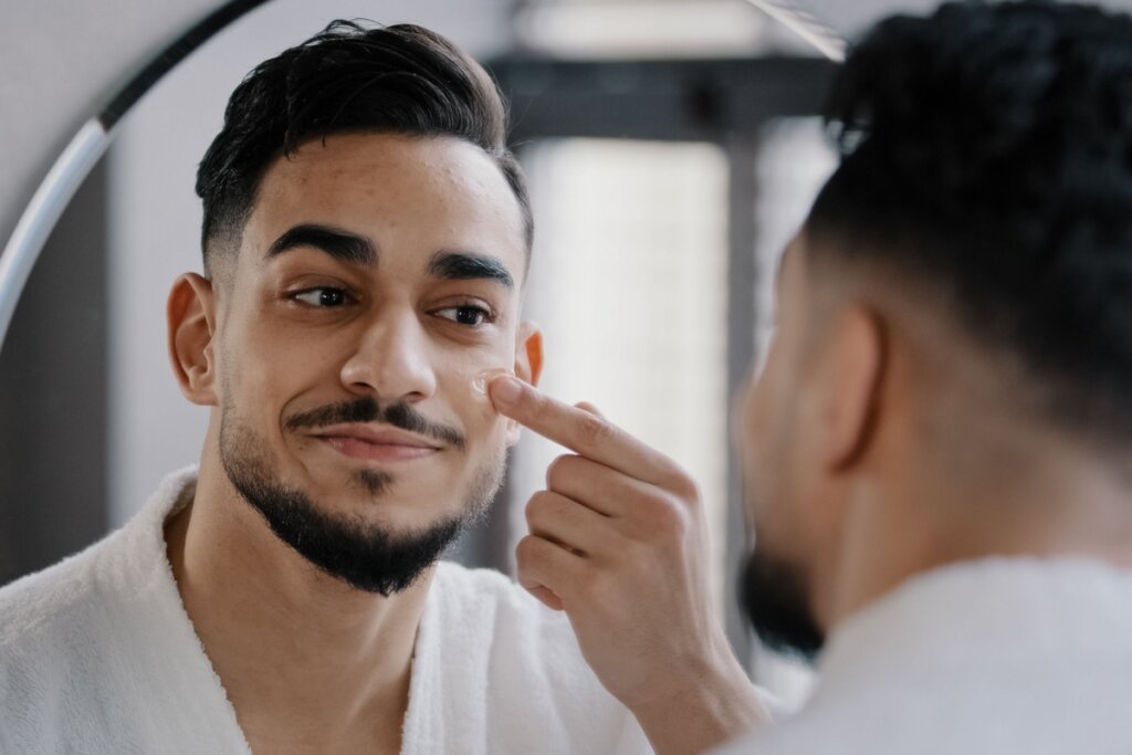 Homem com barba em frente a um espelho fazendo skincare