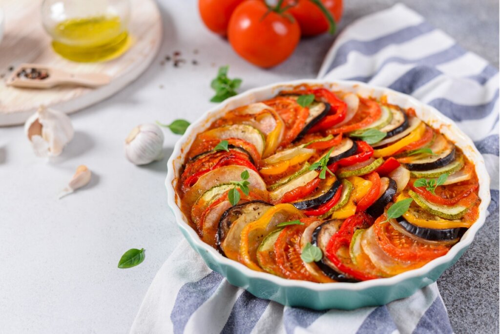 Ratatouille com molho de tomate em uma travessa azul em cima de um pano branco com linhas azuis