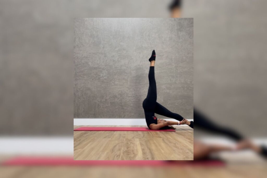 Mulher vestindo roupa preta, apoiada em um tapete de yoga vermelho, fazendo The control balance