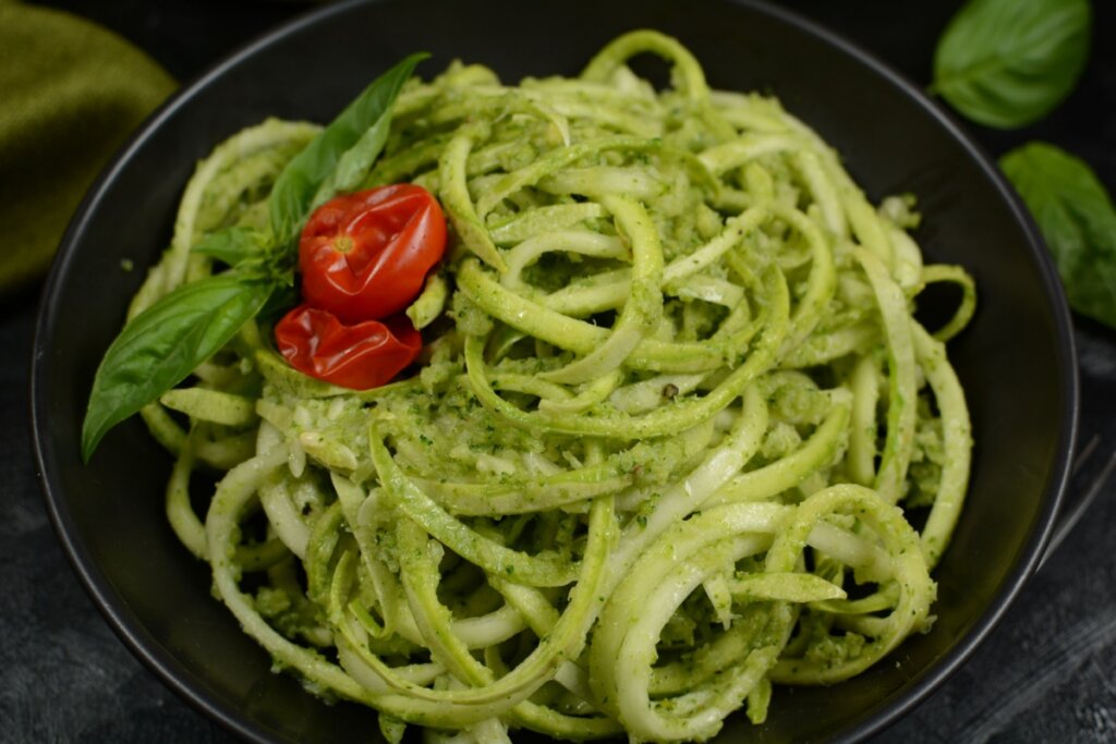 prato preto com espaguete de abobrinha com pesto de manjericão com dois tomates-cereja e folhas de manjericão