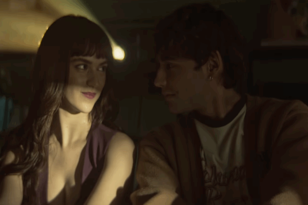 Duas pessoas sentadas lado a lado trocando olhares em um clima de romance