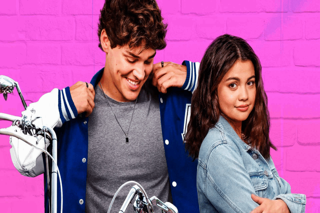 Imagem de um homem usando uniforme de colégio com camisa cinza e casaco azul com detalhes em branco e ao lado uma jovem com cabelo curto, usando jaqueta jeans de braços cruzados, com o guidão de uma moto aparecendo parcialmente em fundo rosa