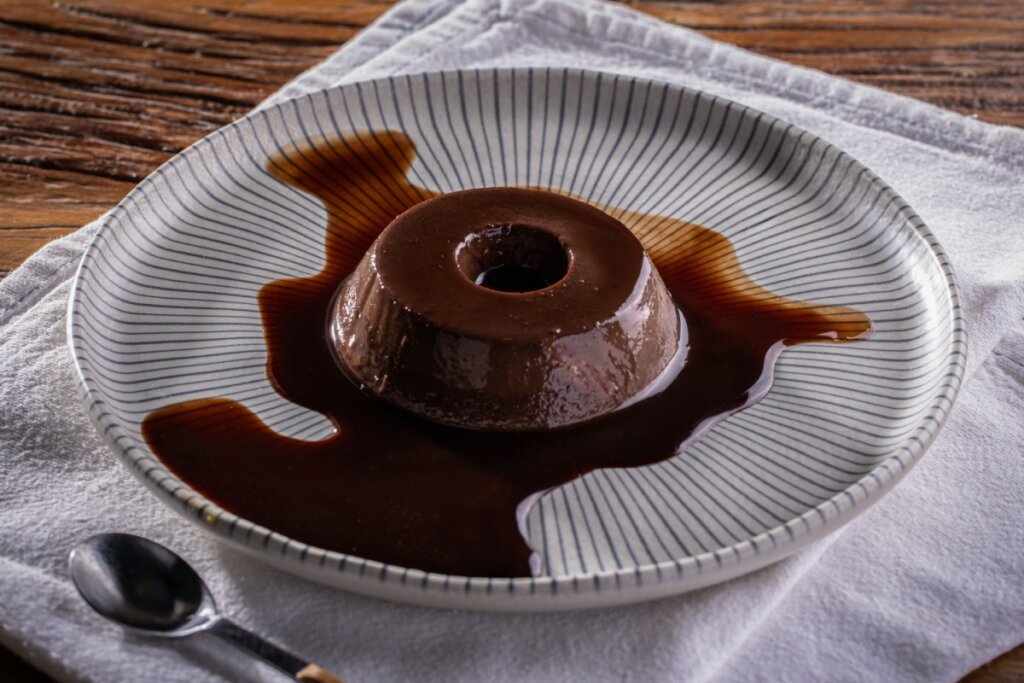 Pudim de chocolate com calda em um prato cinza com linhas pretas 