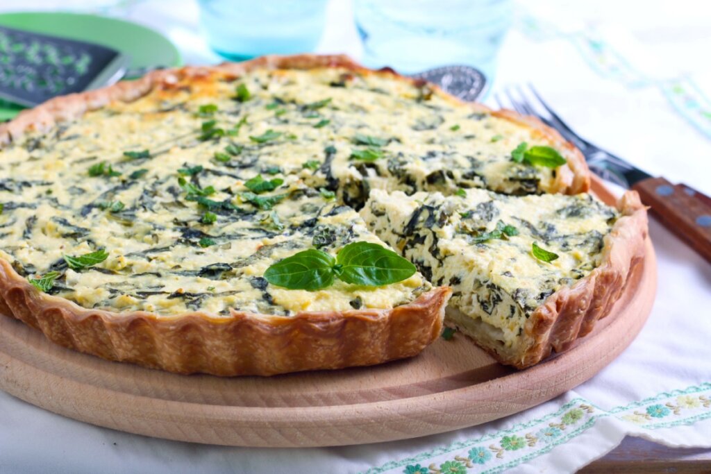 Quiche de espinafre e tofu servido em cima de tábua de madeira em cima de mesa 