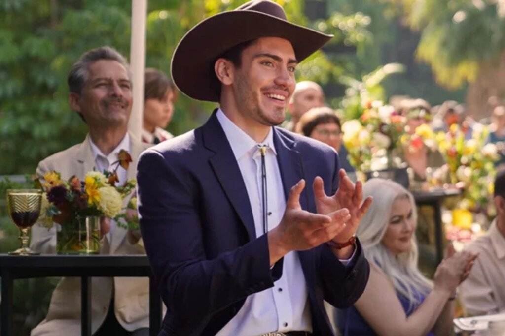 Protagonista de "O Babá", usando terno e chapéu marrom, sorrindo e aplaudindo 