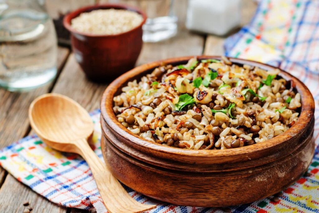 Arroz com lentilha e amêndoas servido em tigela de madeira com colher de pau ao lado em cima de mesa de madeira