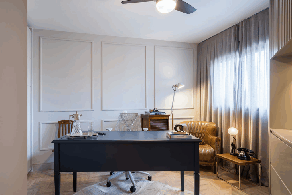 Escritório com parede bege e boiserie da mesma cor, com mesa de trabalho preta e elementos de decoração antigos