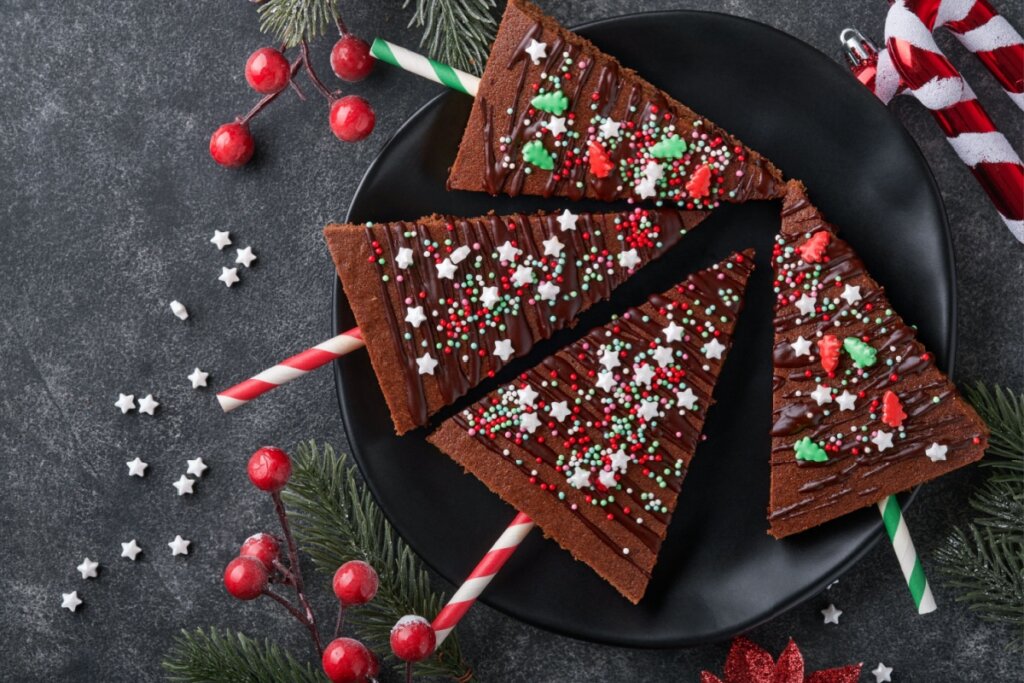 Brownie de chocolate natalino servido em prato de cerâmica preto em cima de mesa de madeira com decoração de natal ao redor