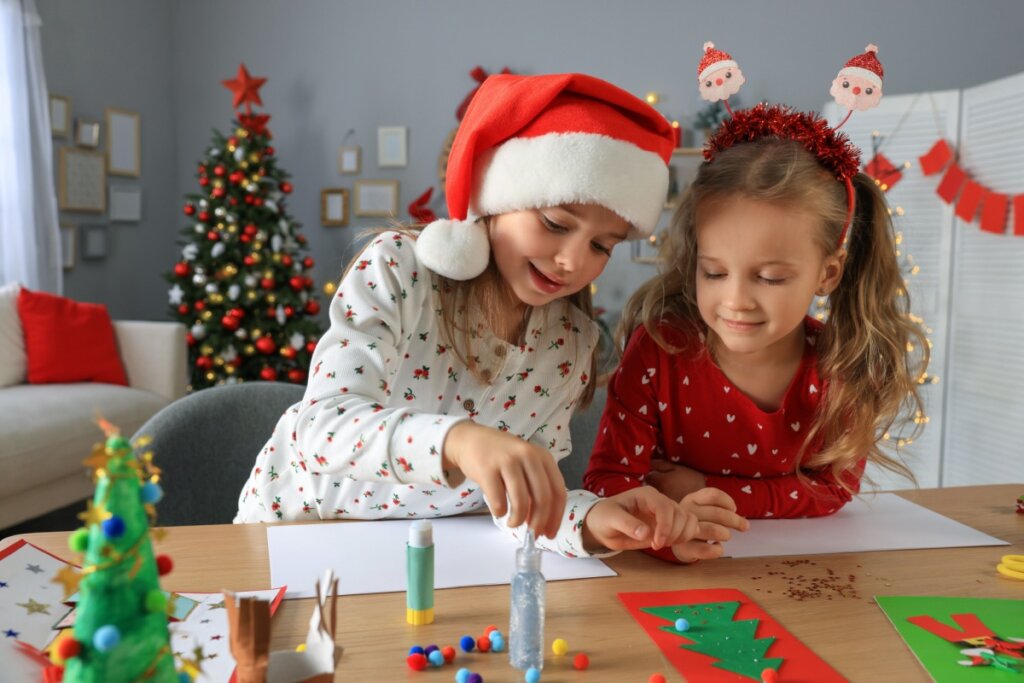 duas meninas em mesa fazendo arte de natal com papel e glitter