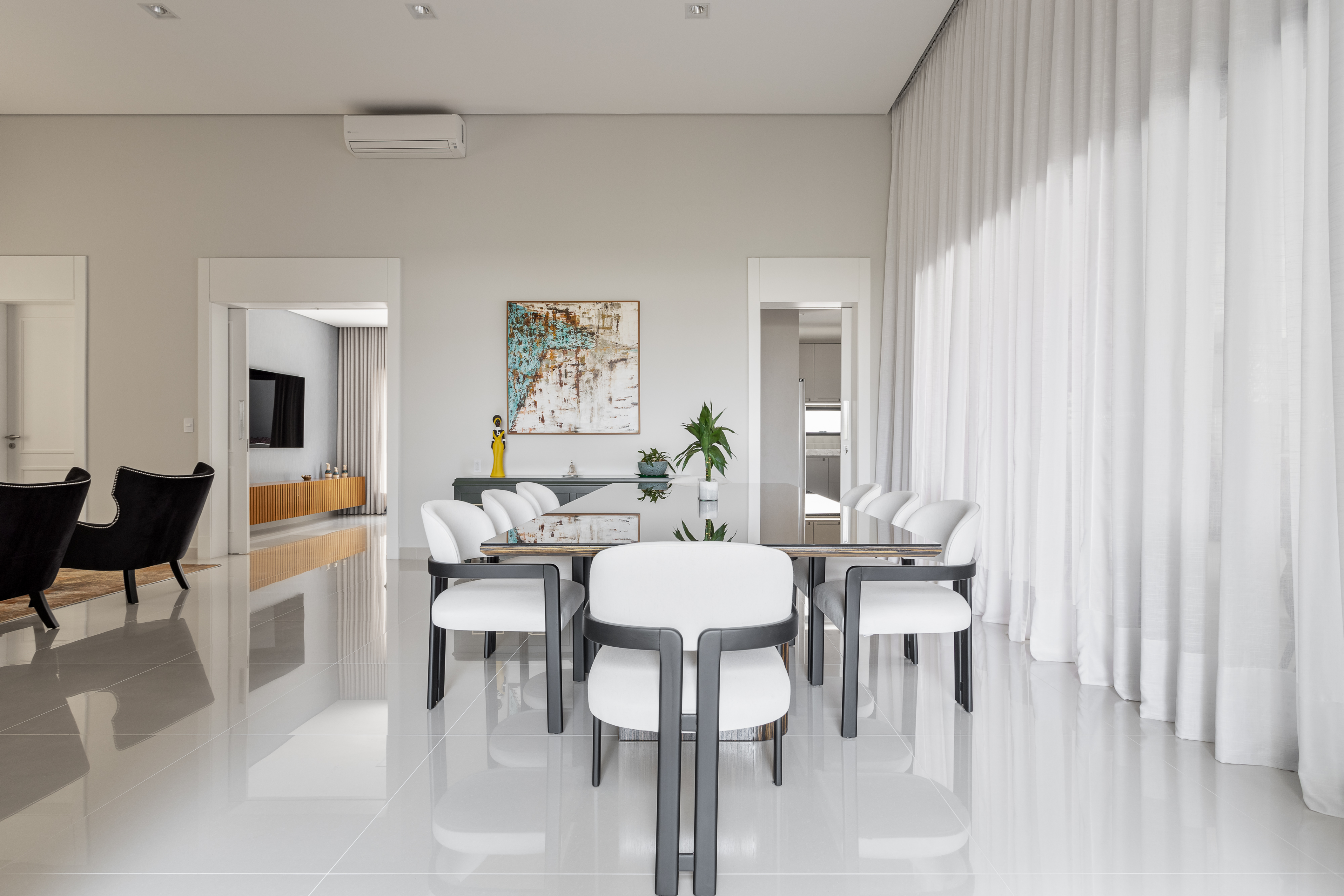 Sala de jantar com cadeiras brancas e mesa com tampo de madeira e vidro com paredes em cores claras